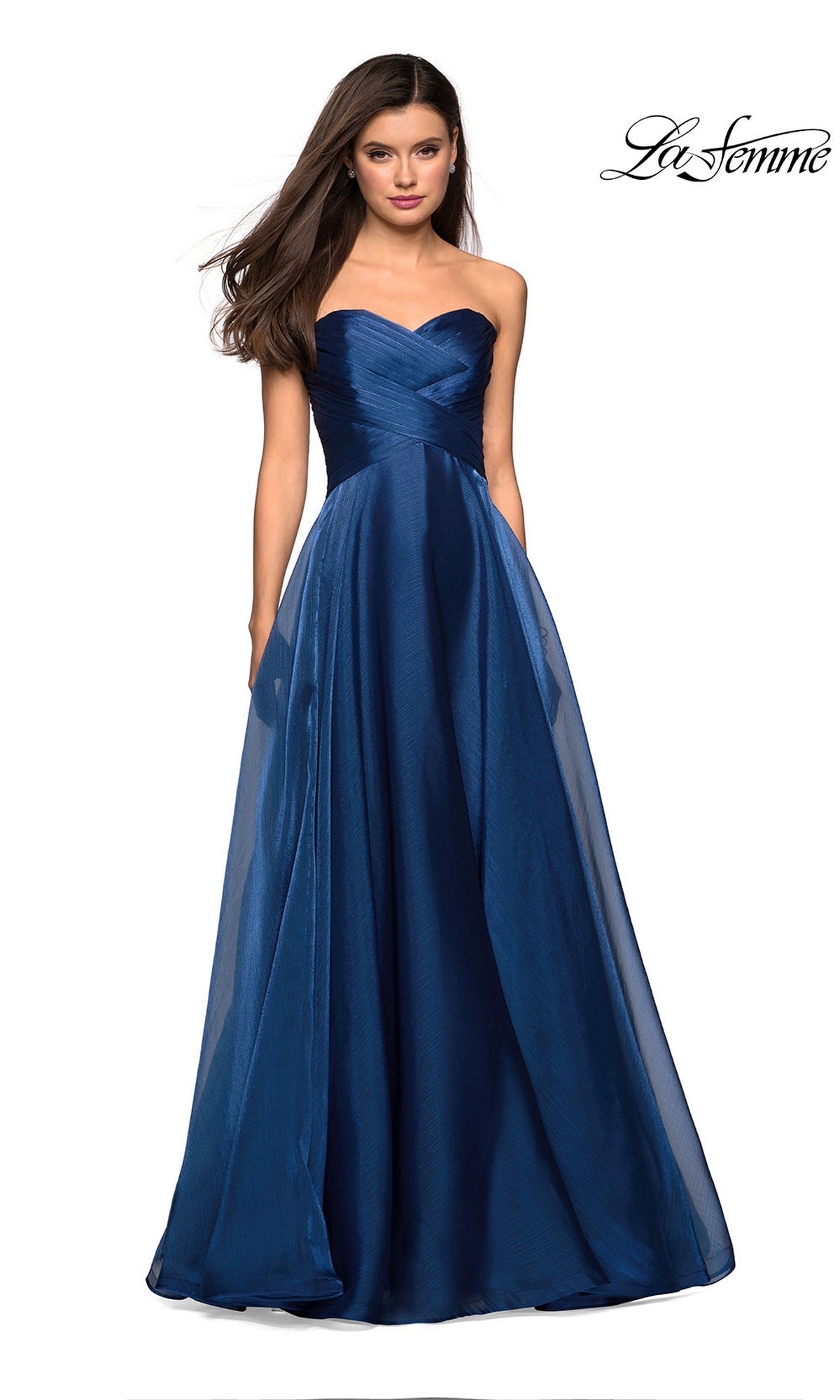 A woman models the La Femme Strapless Long Prom Ball Gown 27515 in navy blue, featuring a fitted bodice and flowing skirt, as she stands against a plain white background.